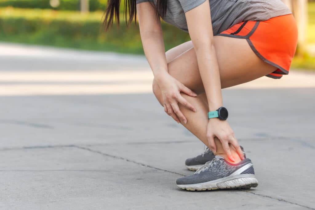 woman crouching down during jog due to achilles pain
