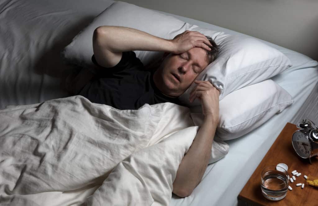 Mature man with hand on forehead in pain while trying to sleep in bed.