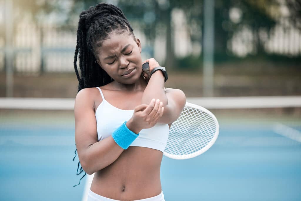 female tennis player holding elbow in pain after injury